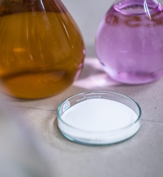 White sodium hydrosulfite powder in a glass dish beside laboratory flasks