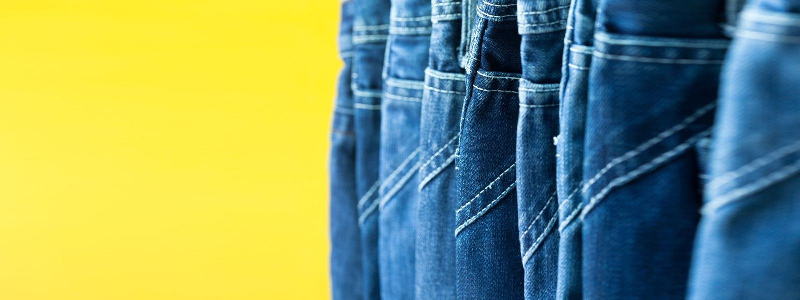 Blue denim jeans hanging against a yellow wall